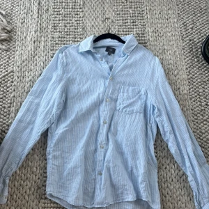 Ljusblå randig linneskjorta från H&M - Säljer en stilren ljusblå randig linneskjorta från H&M i storlek S. Skjortan har långa ärmar och en bröstficka. Perfekt till sommaren och är otroligt populär! Endast använd få gånger så den känns som ny! 