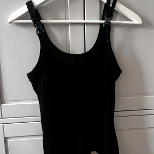 Svart sammetstopp med axelband - Snygg svart sammetstopp med axelband.  Toppen har två detaljer på axelbandet båda dom två har designen försvunnit lite❤️ står ingen storlek men passar som S