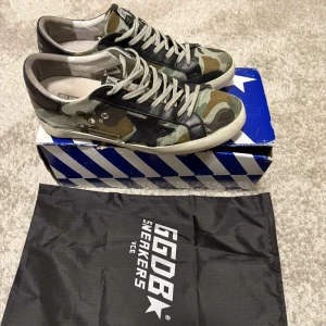 Camo Golden Goose superstar - Tja säljer de här sjukt snygga Camo skorna ifrån golden goose. Skorna säljs inte längre i denhär färgen vilket gör de väldigt ovanliga och svåra att få tag på. Nypris ungefär 5500 kr. Allting OG medkommer. Skick 7/10. De är använda och har ett antal defekter men har fortfarande mycket kvar att ge. Ifall ni undrar över något är det bara att höra av er.