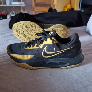 Svarta och guldiga Nike basket skor - Snygga Nike sneakers i svart och guld med snörning. Skorna har en robust sula med bra grepp och en stilren design. Perfekta för  sport.