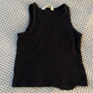 Svart ärmlös topp - Säljer en stilren svart ärmlös topp i mjukt material. Perfekt för varma dagar eller som lager under en jacka. Enkel och mångsidig design.