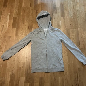 Grå hoodie från Samsøe Samsøe - Säljer en stilren grå hoodie från Samsøe Samsøe. Den har en dragkedja framtill och en bekväm huva. Perfekt för en avslappnad look.