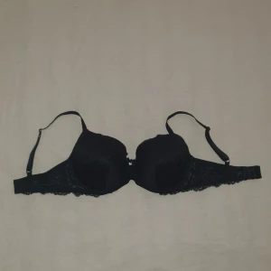 Svart spets-bh med rosett från Hunkemöller - Elegant svart bh med spetsdetaljer och en liten rosett mellan kuporna. Den har justerbara axelband och en slät insida för extra komfort. Perfekt för en stilren look