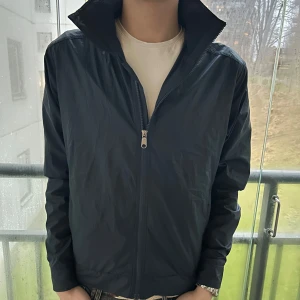 Vindjacka från Peak Performance - Säljer en stilren mörkblå vindjacka från Peak Performance. Jackan har en dragkedja framtill och långa ärmar. Perfekt för blåsiga dagar.