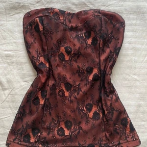 Röd spetsig korsett topp - Snygg röd korsett topp med spets. Den har en elegant passform och är perfekt för att ge en stilfull look. Korsetten är axelbandslös och har en fin struktur som framhäver figuren.