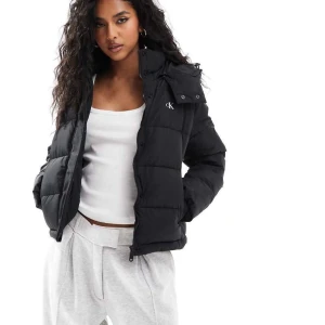 Svart pufferjacka från Calvin Klein - Snygg svart pufferjacka från Calvin Klein med dragkedja och huva. Jackan har en stilren look med CK-logga på bröstet. Passar även S