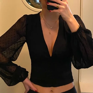 Svart blus/festtopp från BikBok - Snygg svart blus från BikBok med transparenta prickiga ärmar och v-ringning. Blusen har rynkade detaljer framtill och långa ärmar. ❣️ Använd fåtal gånger! 