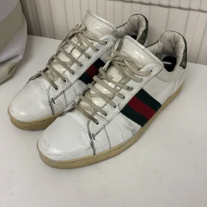Vita sneakers med ränder - Snygga vita sneakers från Gucci  med gröna och röda ränder på sidan. Skorna har snörning och en klassisk design med en slitstark sula. Perfekta för en avslappnad stil. Skick 7/10 lite använda .