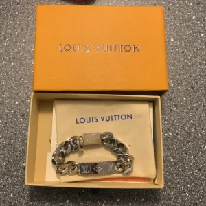 Louis Vuitton armband monogram - KAN TÄNKA MIG BYTE MOT FETA SKOR ELLLER CARDIGAN!!!! Säljer ett stilrent silverfärgat armband från Louis Vuitton. Armbandet har en robust kedjedesign med märkets ikoniska logotyp ingraverad. Perfekt för att ge en lyxig touch till din stil. Levereras i originalförpackning med tillhörande dokumentation. 