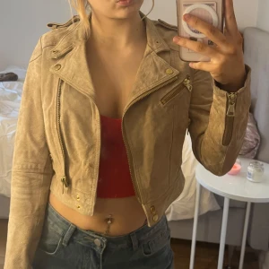 Beige mockajacka - Snygg beige mockajacka med dragkedja och knappar. Jackan är croppad och har långa ärmar med dragkedjor vid ärmsluten. Perfekt för en stilren look. Köpt begagnad för något år sedan, men jag har aldrig använt den. 