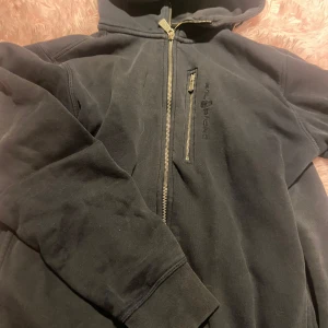 Blå huvtröja från Sail Racing - Säljer en blå huvtröja från Sail Racing med dragkedja framtill. Tröjan har långa ärmar och en praktisk huva. Den har även ett hål i armen och slitna längst ut därav priset. Passar för både män och kvinnor! 