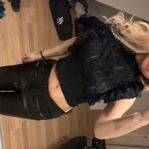 Svart spetsblus - Snygg svart blus med spetsdetaljer och volanger. Den har korta ärmar och en croppad passform som ger en trendig look. Perfekt för att piffa upp vilken outfit som helst.