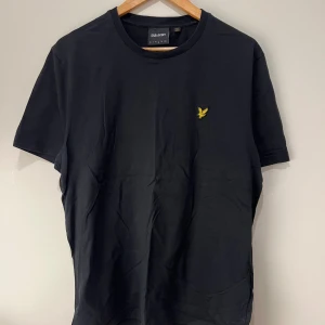 Svart t-shirt från Lyle & Scott - Säljer en stilren svart t-shirt från Lyle & Scott med deras ikoniska gula logga broderad på bröstet. Tröjan har använts ett par gånger men är i bra skick, samt inga tecken på slitage! 