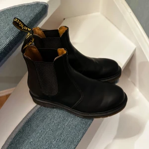 Svarta Chelsea boots från Dr. Martens - Snygga svarta Chelsea boots från Dr. Martens med klassisk gul dragflik och elastiska paneler på sidorna. Perfekta för en stilren look med robust sula för extra komfort och hållbarhet. Använda 1 gång. Pris kan diskuteras 