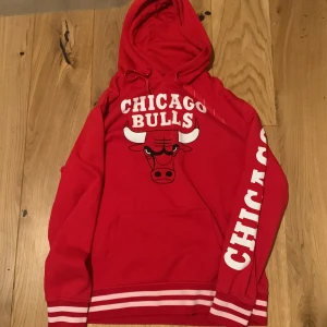 Röd Chicago Bulls hoodie - Snygg röd hoodie med Chicago Bulls-logga och text på bröstet och ärmen. Den har en klassisk känguruficka och ribbade muddar i vitt och rött. Perfekt för fans av laget eller basket! XL men passar L - M. Pris ej hugget i sten och våga fråga! 😊😁