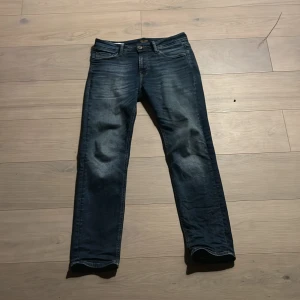 Blå jeans från Jack & Jones - Snygga blå jeans från Jack & Jones med en klassisk femficksdesign och knappgylf. De har en regular fit och är perfekta för en avslappnad stil. Jeansen har en lätt tvättad look som ger dem en cool vibe.