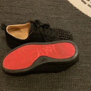 Svarta Louboutins - Snygga svarta Loubs med nitar på tån och en iögonfallande röd sula. Skorna har snörning och en stilren design som passar perfekt för den som vill sticka ut.