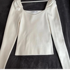 Vit långärmad topp från NA-KD - Säljer en stilren vit långärmad topp från NA-KD. Toppen har en v-ringad design och är tillverkad i ett mjukt material som ger en bekväm passform. Perfekt för både vardag och speciella tillfällen.