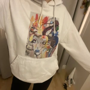 Vit hoodie med konstnärligt tryck - Säljer en vit hoodie med ett färgglatt och konstnärligt tryck på framsidan. Hoodien har en stor ficka framtill och justerbara snören i huvan.💕