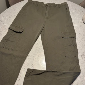 Olivgröna cargobyxor - Säljer ett par olivgröna cargobyxor med flera praktiska fickor och knappstängning. Perfekta för en avslappnad och funktionell stil. Raka ben.
