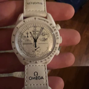 Vit klocka från Omega x Swatch - Snygg vit klocka från Omega x Swatch snoopy edt. Knappt använd inga repor eller märken. Original box med alla papper följer med. Nypris 7-8000