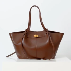 Brun skinnväska med gulddetalj - Säljer en snygg brun skinnväska i mycket bra skick. Väskan har en elegant gulddetalj på framsidan och långa handtag som gör den perfekt som axelväska. Den är rymlig. Passar till alla säsonger och outfits! Men den har tyvärr gått lite sönder vid ett av handtagen, be om bild vid frågor. Så den enda defekten är en liten skinn bit som inte sitter kvar, sen har det blivit sprickor kan man säga på sidorna för skinnet håller på att tappas. Vatten fläckar i väskan