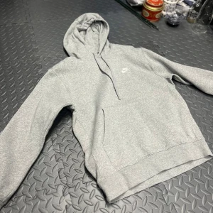 Grå hoodie från Nike - Säljer en klassisk grå hoodie från Nike i storlek S. Den är superbekväm och perfekt för både chill och träning. Hoodien har en känguruficka och Nike-loggan broderad på bröstet. Perfekt för höst och vår!