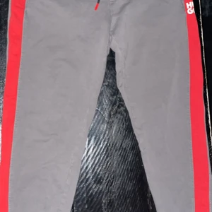 Grå mjukis byxor med röd detalj från Hugo - Kan snacka om priset! Snygga grå byxor med röd sidodetalj och Hugo-logga. Perfekta för en stilren look med en touch av färg. Riktigt sköna och funkar till en vardaglig stil men funkar även om man vill vara lite extra snygg hemma när man bara chillar med sina kompisar, funkar även på gymmet eftersom de är perfekt stretchigt material och lite baggy men ändå inte.