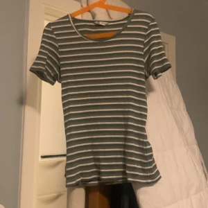 Randig t-shirt i grönt och vitt - Säljer en snygg randig t-shirt i grönt och vitt från märket Cubus. Den är kortärmad och har en normal passform, perfekt för både vår och sommar. Materialet känns mjukt och bekvämt, idealiskt för vardagsbruk. Passar perfekt till vida byxor eller till jeans. Sitter ganska tight.