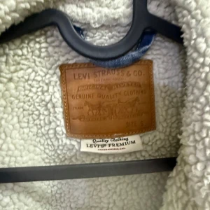  Levi's jacka - Säljer en snygg jeansjacka från Levi's i bra skick. Den har ett mysigt teddyfoder som gör den perfekt för höst och vår. Jackan är ljusblå med klassiska knappar och två bröstfickor. Perfekt för en casual look!