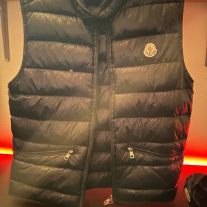 Moncler Gui Navy - Moncler Gui stl 3 i Navy Blue. Fint skick, inga revor/fläckar. Gammal modell, inköpt typ 2010 om jag inte minns fel. Påse hänger med.                Tyvärr har dragkedjan börjat släppa lite så kan vara lite klurig att stänga, se bild. Går att åtgärda men inget jag har lust att göra då den ej används.