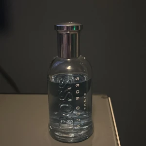 Hugo Boss Tonic Parfym - Fräsch och energigivande parfym från Hugo Boss med citrus och varma kryddiga noter. Flaskan är elegant med en stilren design i blått glas och silverfärgad kork. Perfekt för den som vill ha en uppfriskande doft med inslag av frukt och trä.  Ca 80ml kvar