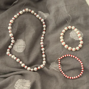 Pärlset med halsband och armband i rött och vitt till jul - Charmigt pärlset bestående av ett halsband och två armband. Gjort till min hemsida men säljer det även här. Halsbandet och ett av armbanden har vita pärlor med små röda detaljer, medan det andra armbandet har ett mönster av röda och vita pärlor. Perfekt för att ge en färgklick till din outfit.