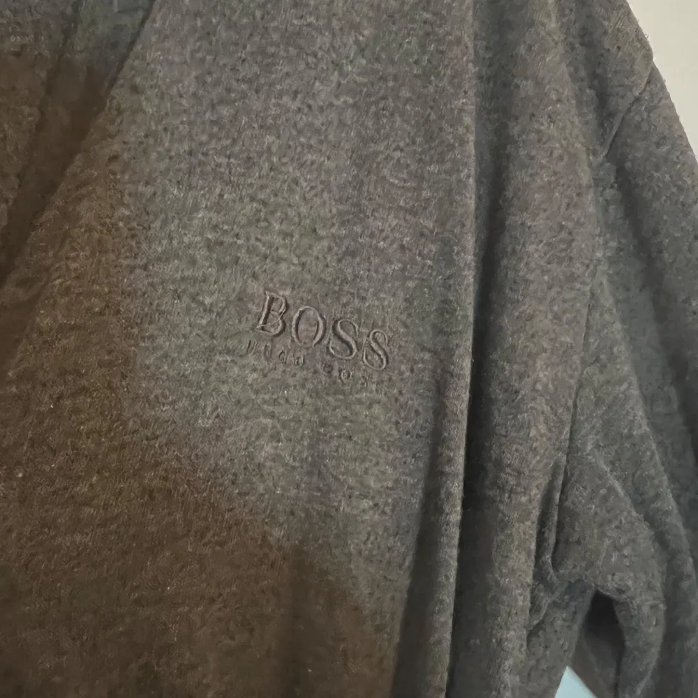 Säljer en grå lång kofta från Boss med knytband i midjan. Rocken har långa ärmar och ett subtilt Boss-märke på bröstet samt längs ärmen. Perfekt för bekväm look.. Muu.