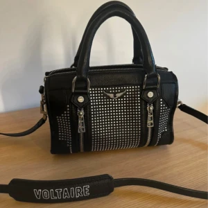 Svart handväska från Zadig & Voltaire - Snygg svart handväska i skinn från Zadig & Voltaire med silverfärgade nitar och dragkedjor. Väskan har både handtag och en avtagbar axelrem. Köpt i Zadig butiken i Sthlm. Köpt för 5050kr, men har lite tecken på användning därav priset. Inget som syns eller som man tänker på annars😊😊 Kvitto och dustbag ingår 