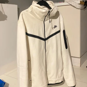 Vit hoodie från Nike - Säljer en stilren vit hoodie från Nike med dragkedja och huva. Den har svarta detaljer och en ficka på ärmen.  Super bra kvalité.