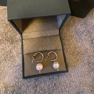 Maria Nilsdotter örhängen - De populära  silverörhängen från Maria Nilsdotter med hängande vita pärlor. Finns inga tecken på slitage väldigt försiktigt andvända, kan sälja styck, skriv isf till mig privat för pris