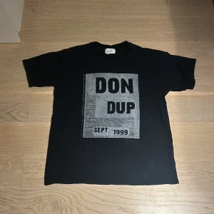 Svart t-shirt från Dondup - Snygg svart t-shirt från Dondup med tryck 'DON DUP SEPT. 1999' på framsidan. Tillverkad i Italien, perfekt för en stilren look. Skicket är alldeles prima. OBS storleken som står att den är XS motsvarar ungefär M/L.