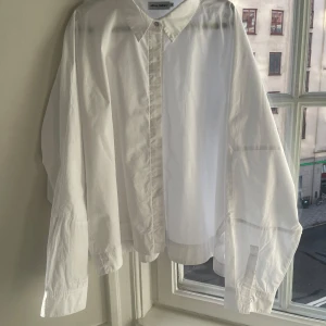 Vit skjorta från Ahlvar gallery  - Säljer en stilren vit skjorta från Ahlvar gallery  i storlek L. Skjortan har en klassisk krage och knappar framtill. Oversized och något croppad. Använd endast fåtal gånger pga fel storlek. Perfekt för både vardag och fest! 🕺snygga till jeans och funkar som overshirt också. Kostar 1.595kr i affär. 