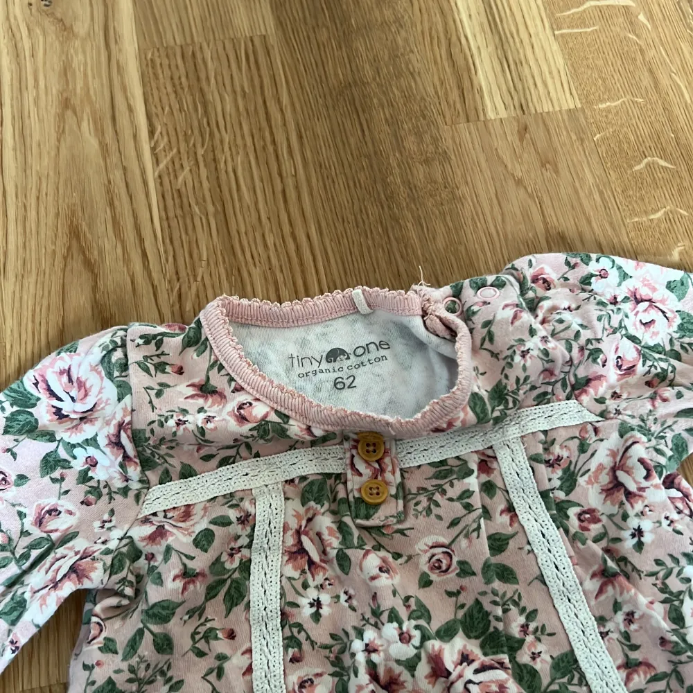 Söt blommig klänning i rosa och grönt från Tiny One. Tillverkad i ekologisk bomull med trekvartsärmar och volangdetaljer. Perfekt för små fashionistas!. Mekot.