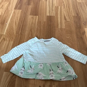 Randig långärmad topp med kaninmotiv - Söt långärmad topp från Pytteliten i mintgrönt och vitt med randigt mönster. Den har ett volangliknande parti med kaninmotiv längst ner. Perfekt för små äventyrare!