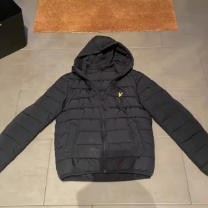 Marinblå pufferjacka från Lyle & Scott - Säljer en snygg marinblå pufferjacka från Lyle & Scott i storlek S. Jackan har en huva och dragkedja framtill. Perfekt för kyliga dagar med sin quiltade design. Den är i mycket bra skick och redo för nya äventyr! 