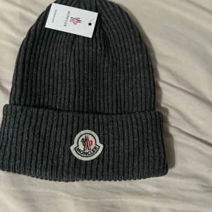 Moncler Mössa - Säljer en snygg grå ribbad mössa från Moncler. Den är i nytt skick.