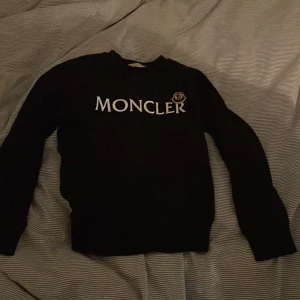 Svart tröja från Moncler - Säljer en snygg mörkblå tröja från Moncler med deras ikoniska logga på bröstet. Tröjan är i mycket bra skick och perfekt för både höst och vinter. Den har långa ärmar och är gjord i ett mjukt material som håller dig varm. Perfekt för dig som vill ha en stilren look! 🖤