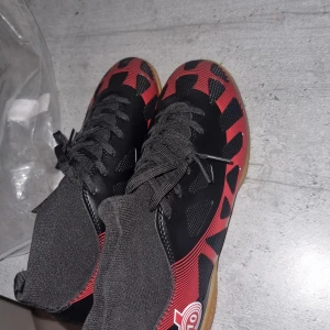 Svarta och röda fotbollsskor/ för kampsport  - Snygga fotbollsskor i svart och rött med snörning och mönstrad design. Skorna har en gummisula som ger bra grepp på planen.