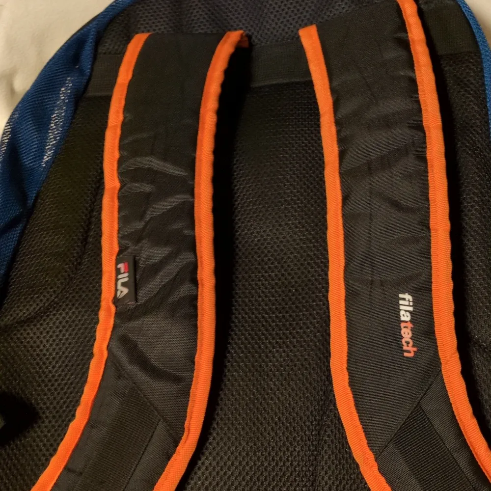 Snygg blå ryggsäck från Fila med orange detaljer och flera praktiska fack. Perfekt för skolan eller träningen. Justerbara axelremmar för extra komfort och en robust dragkedja för säker förvaring.. Laukut & Käsilaukut.