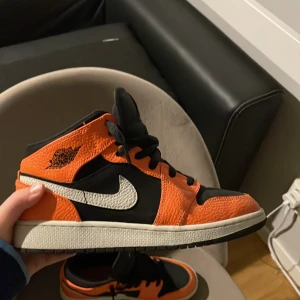 Nike Air Jordans i orange och svart - Snygga Nike Air Jordans i en fräck kombination av orange och svart. Skorna har en klassisk design med snörning och den ikoniska Nike-loggan på sidan. Perfekta för dig som vill sticka ut. 100% äkta