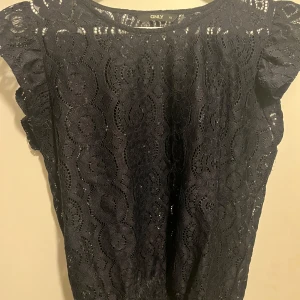 Marinblå spetsblus från ONLY - Snygg marinblå spetsblus från ONLY i storlek XS. Blusen har korta ärmar och ett vackert spetsmönster som ger en elegant touch. Perfekt för både vardag och festliga tillfällen. Skriv för fler bilder❣️