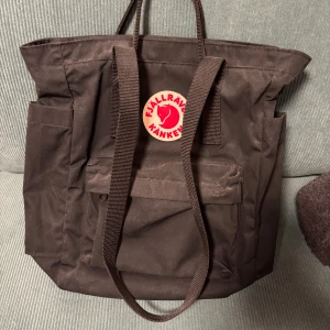 Svart ryggsäck från Fjällräven - Säljer en snygg svart ryggsäck från Fjällräven i mycket bra skick. Den har ett klassiskt Kånken-märke på framsidan och praktiska axelremmar. Perfekt för både vardag och utflykter. Ryggsäcken har en stilren design och är gjord i slitstarkt material. Den är dammig då den bara hängt på dörren länge! 