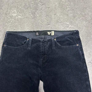 Svarta manchesterbyxor med slits - Snygga svarta manchesterbyxor med låg midja och slitsdetaljer vid bensluten. Från GUESS. Innerbenslängd: 87cm midjemått: 40cm